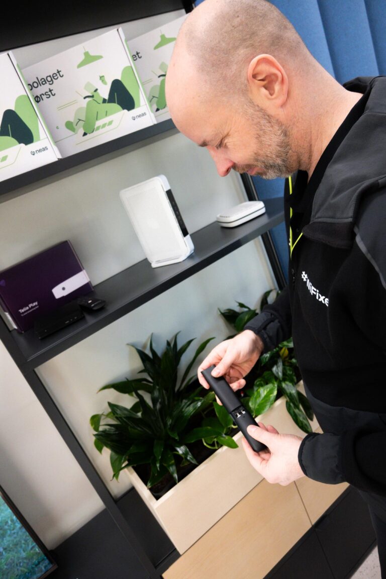 Mann står med fjernkontroll i hånda, i bakgrunnen er det ei hylle med en TV-boks og WIFI-ruter