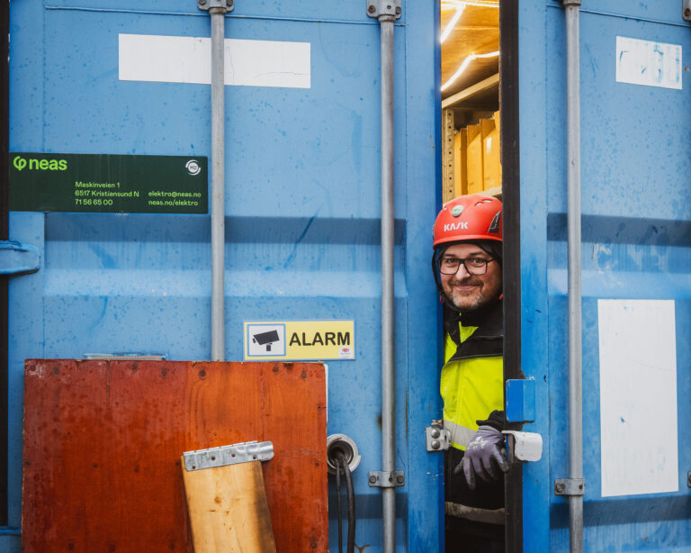 Elektriker ser ut fra container med Neas-klistremerke